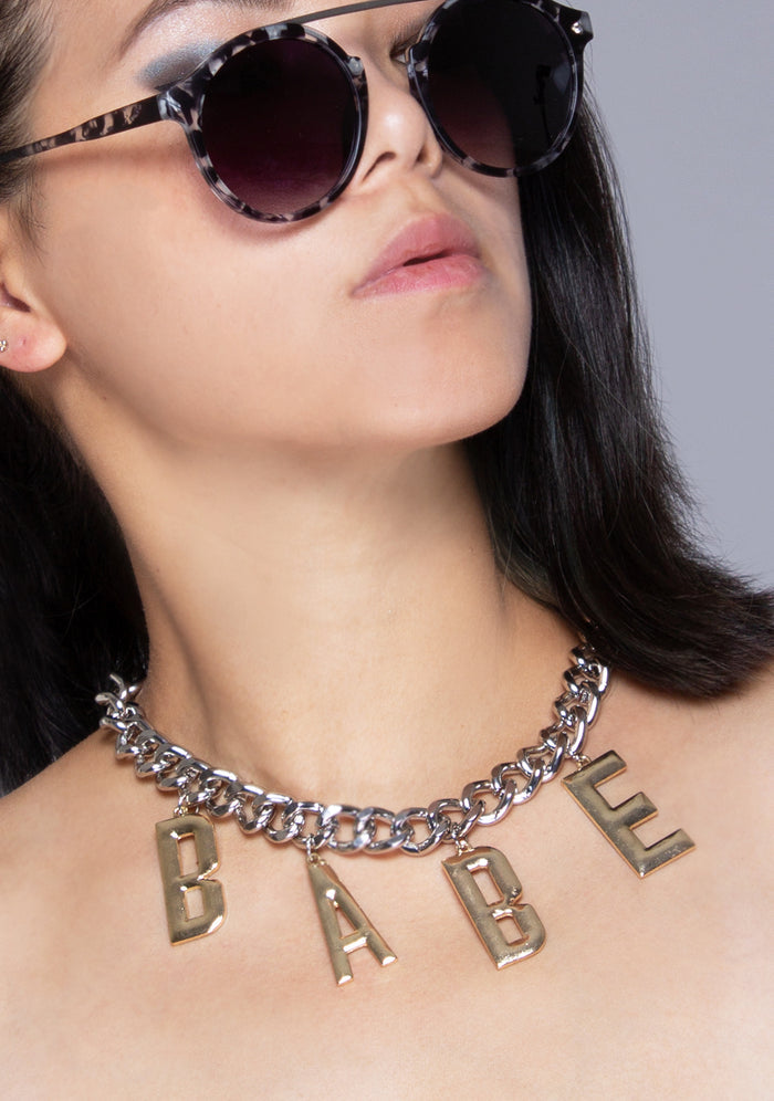 8 Other Reasons Babe Status Necklace in gold with chunky Babe letter charm pendant on gold chain festival necklace — model view