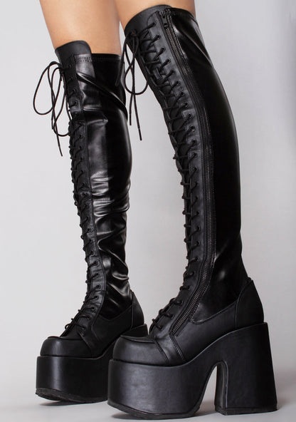 Demonia CAMEL 300 Rude Awakening Thigh-High Black Platform Boots in black vegan leather with elasticized stretch upper and lace-up front worn by model — side view