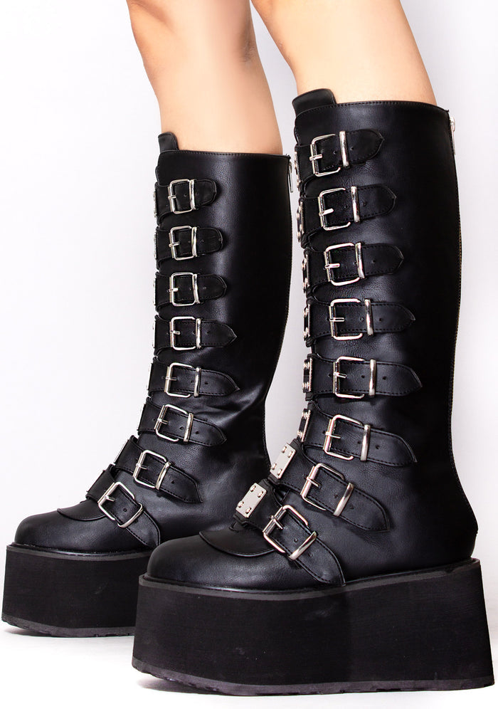 Demonia DAMNED 318 Obsession Black Platform Boots in black vegan leather with buckle strap front and traction sole worn by model — side view