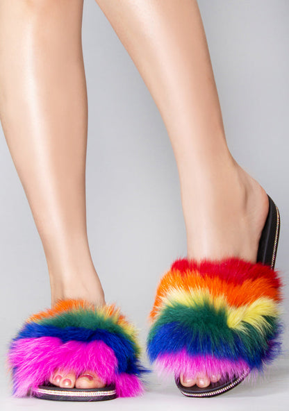 Side profile view of the rainbow faux fur festival sandals on-model, highlighting the flat slip-on design and the glittering rhinestone trim along the sole.
