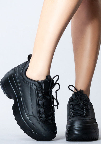 Front view of the black LILY 5005 Next Level platform sneakers on-model, showing the clean tongue design, black laces, and wide toe box.