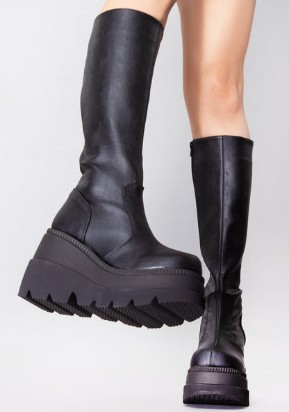 Demonia SHAKER 100 Total Blackout Black Platform Boots in black vegan PU leather with interior zip closure worn by model — side view