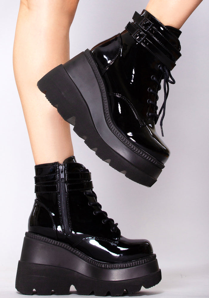 Demonia SHAKER 52 Paint it Black Patent Black Platform Boots in black patent leather with strap buckle front and lace-up closure worn by model — side view