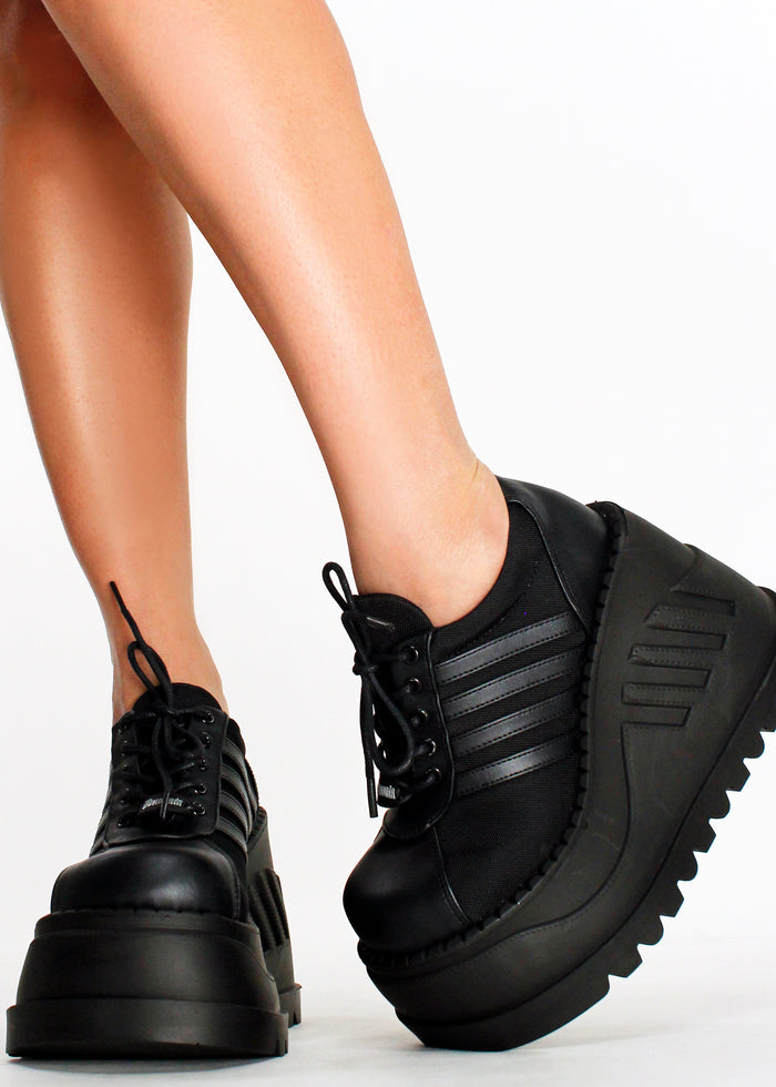 Demonia STOMP 08 Black Rave Platform Sneakers in black vegan leather with sporty stripe and major traction outsole worn by model — front view