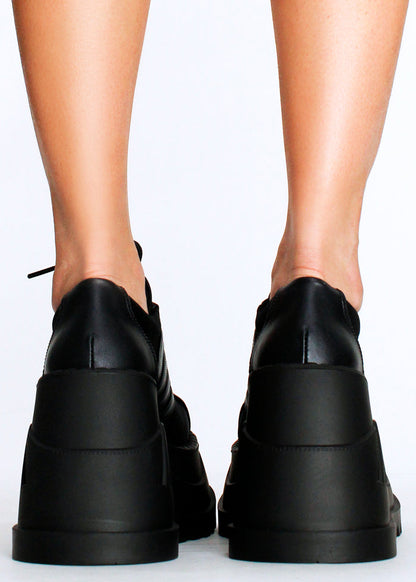 Demonia STOMP 08 Black Rave Platform Sneakers in black vegan leather with chunky rubber wedge platform worn by model — back view