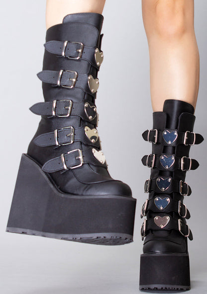 Demonia SWING 230 Black Heart Black Platform Boots in black vegan leather with heart buckle strap detail worn by model — side view