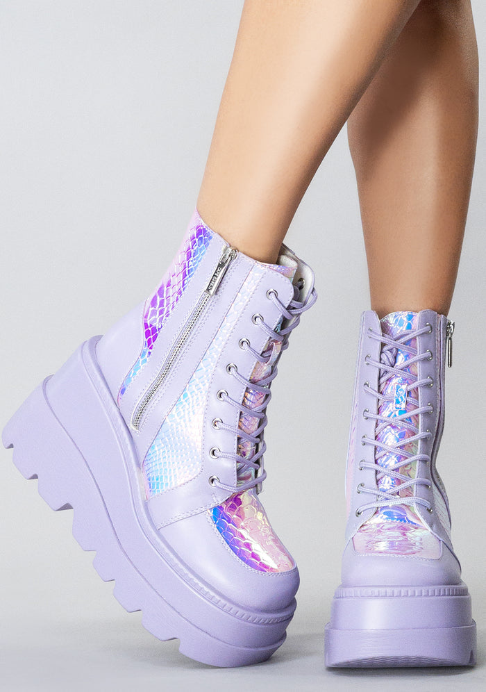 Side angle view of the lavender RADIO rave platform boots on-model, highlighting the contrast of the shimmering iridescent python texture panels under bright lighting.