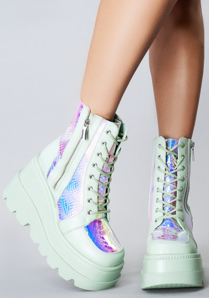 Side angle view of the mint green RADIO rave platform boots on-model, highlighting the contrast of the shimmering iridescent python texture panels under festival lighting.